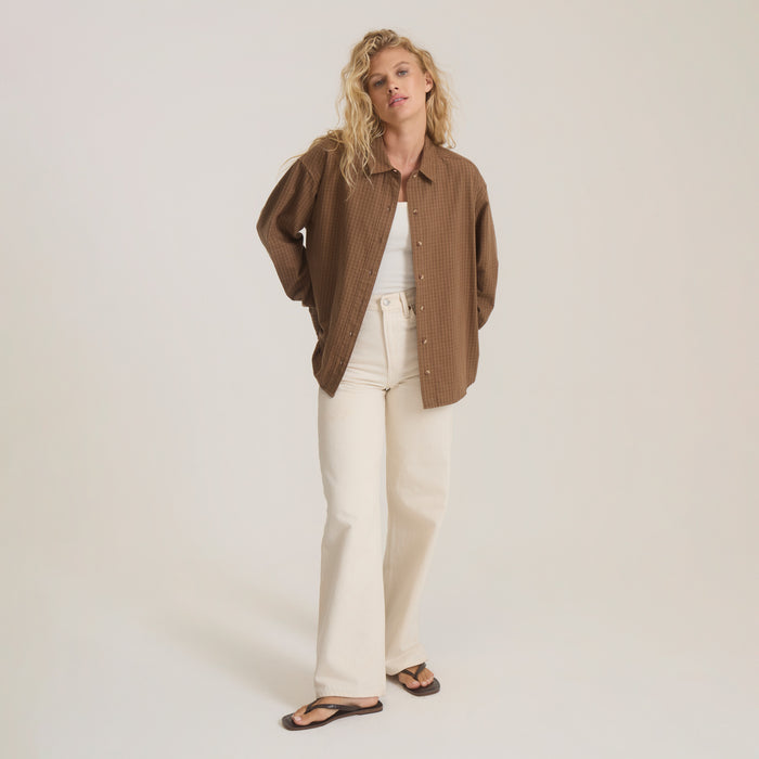 Brown checkered button up shirt on model styled with white pants and black sandals against neutral background