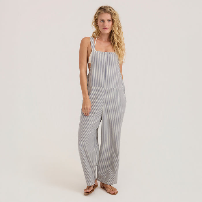 Blond model wearing a one-piece overall in a rustic outdoor setting, embodying Roark's spirit of adventure and travel.