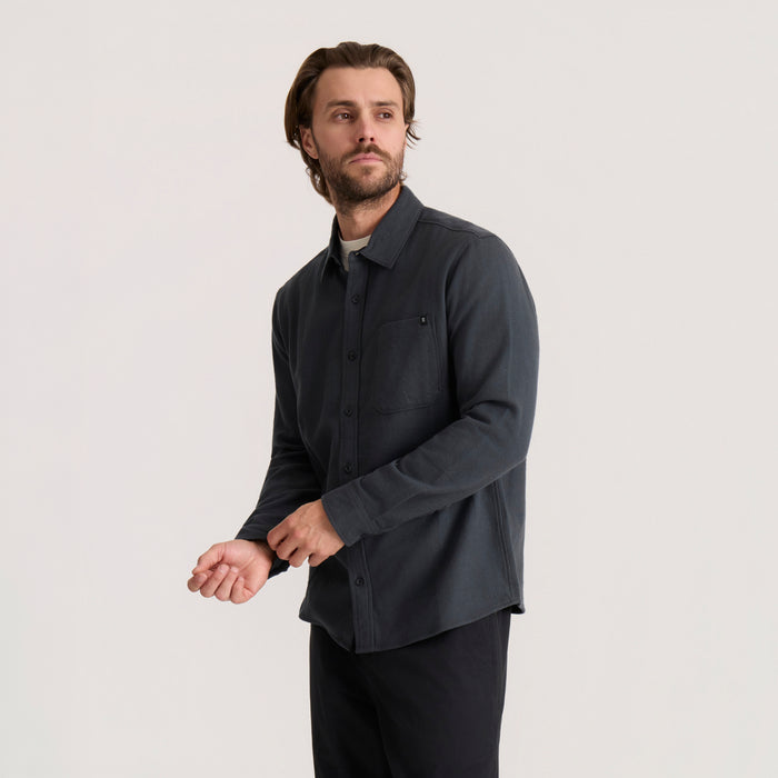 Dark charcoal organic cotton flannel shirt on male model, long sleeves with button front and chest pocket, worn with black pants
