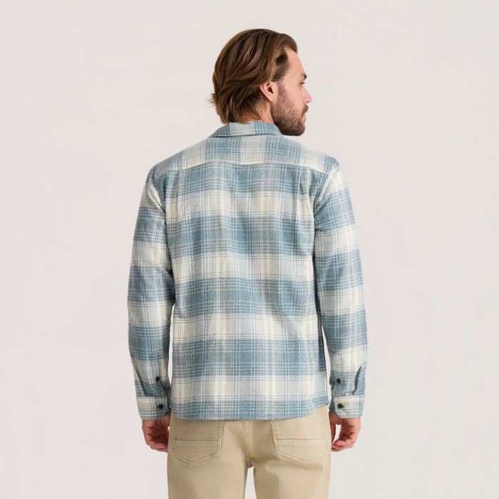 Man wearing blue and cream plaid flannel shirt with long sleeves, shown from back view against neutral background