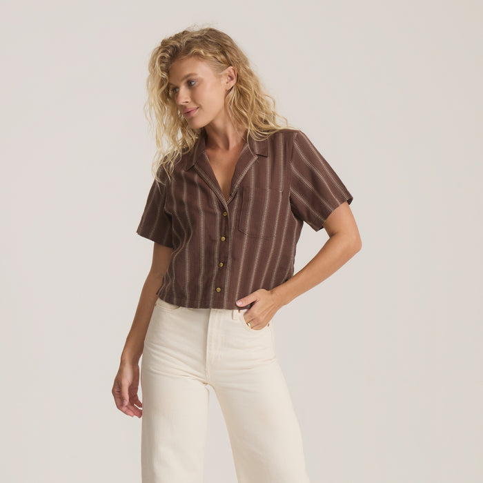 Brown striped short-sleeve camp shirt with button front worn with cream pants on model