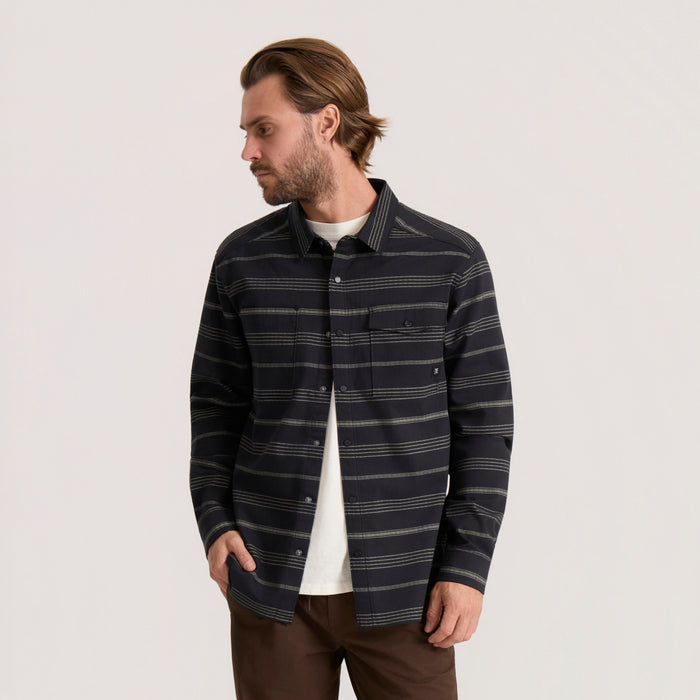 Man wearing black striped long sleeve flannel shirt over white tee with brown pants, shown in profile view