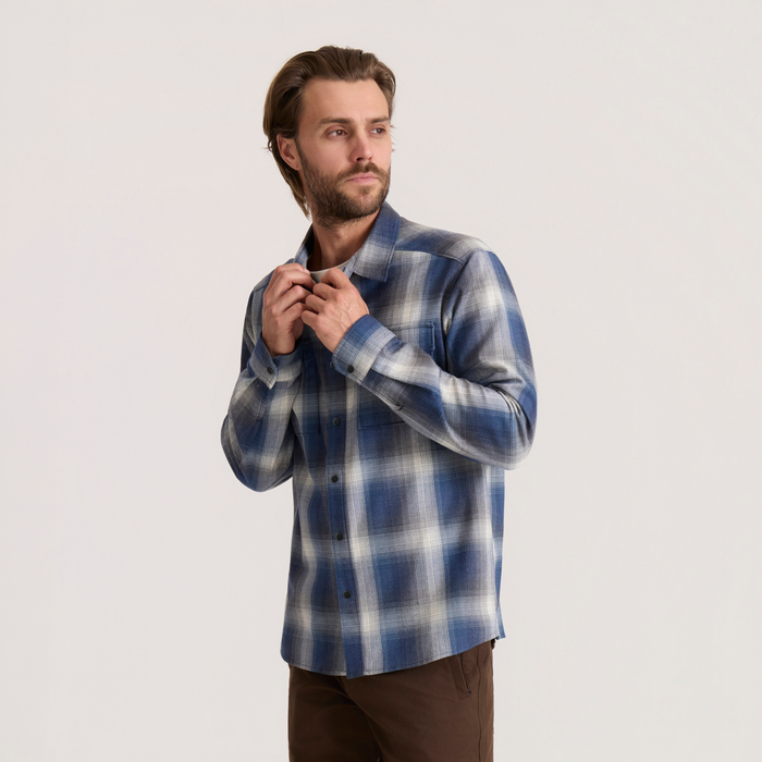 Man wearing Diablo long sleeve flannel in slate blue and white plaid pattern with brown pants, standing against neutral background