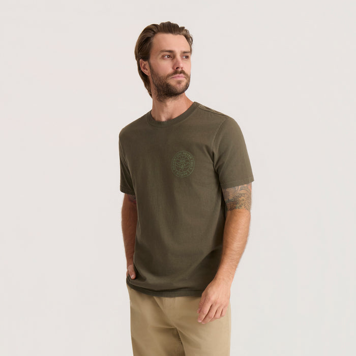 Olive green Division Premium Tee with circular chest logo worn by man on neutral background, paired with khaki pants