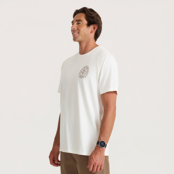 Man wearing off-white Division Premium Tee with small chest logo, paired with tan shorts, shown in profile view