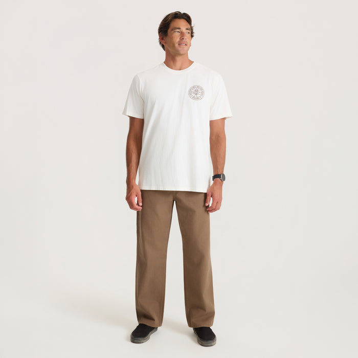 Man wearing off-white Division Premium Tee with chest logo, paired with tan pants and black sneakers, standing against neutral background