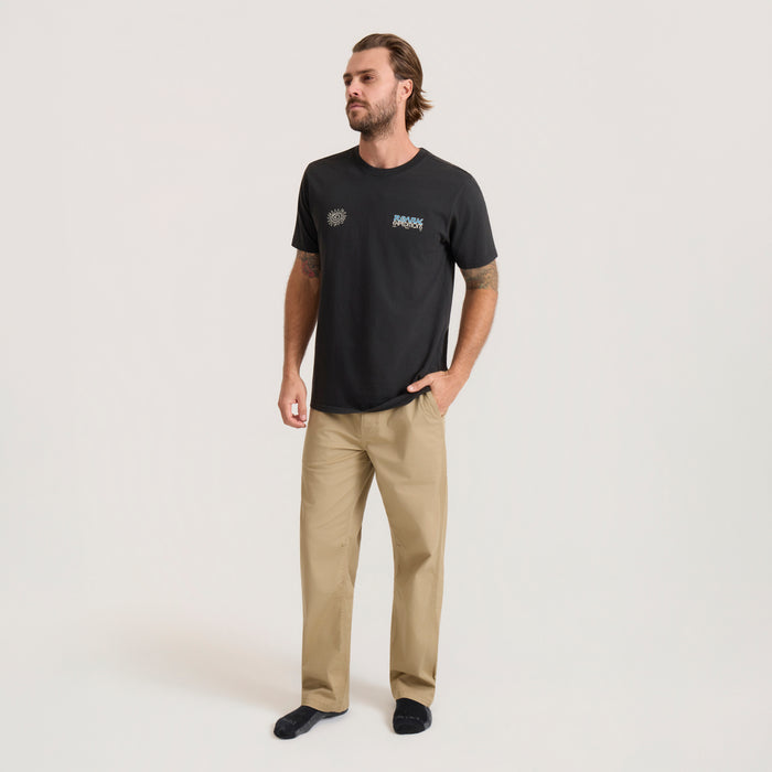 Man wearing black Elevated Research Premium Tee with chest logo and beige pants, standing against neutral background