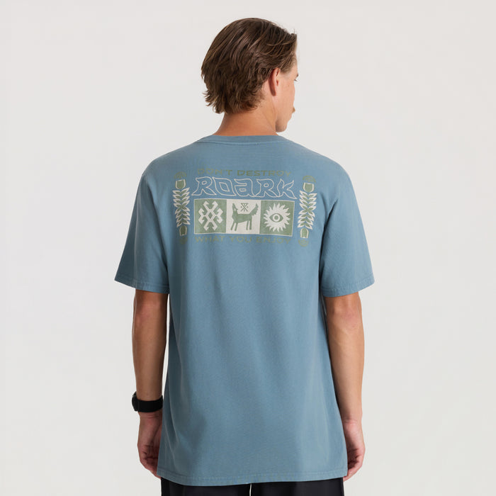 Slate blue short sleeve tee with Roark graphic print on back, displayed on male model from behind against neutral background