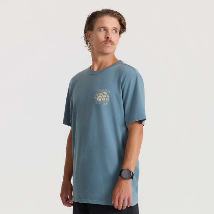Man wearing slate blue short sleeve tee with small graphic print, styled with black shorts and dark watch