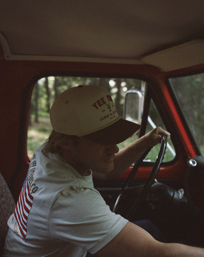Person driving a vintage vehicle with a 'Yee Yee' cap inside.