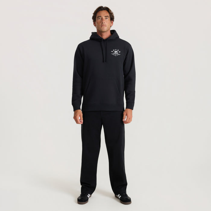 Man wearing black Fear The Sea hoodie with embroidered logo on chest, paired with black sweatpants, standing against neutral background