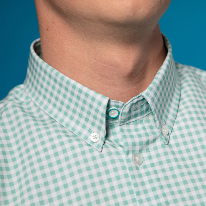 Man wearing light green and white gingham shirt. Top button is blue.