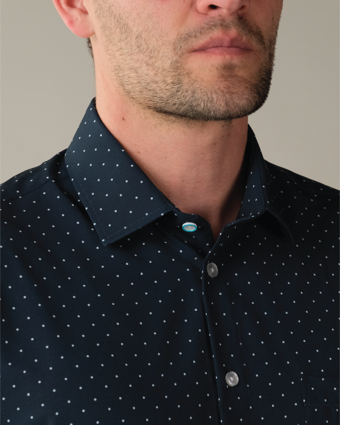 Man wearing navy shirt with white polka dots. Top button has blue ring.