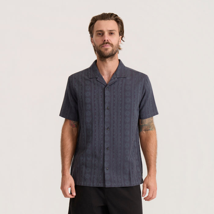 Dark gray short sleeve button up shirt with subtle geometric pattern worn by man against neutral background