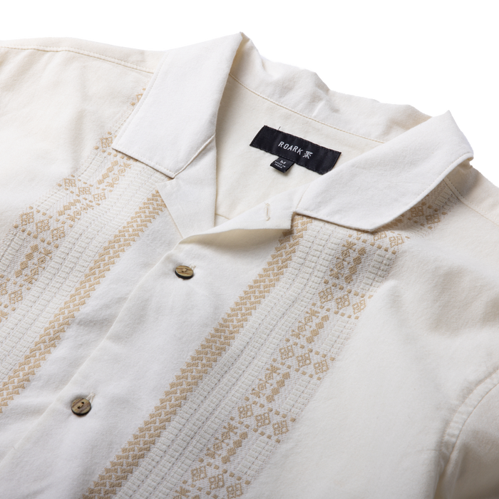 Cream short sleeve button up shirt with tan geometric embroidery stripes down the front and collar detail, flat lay view