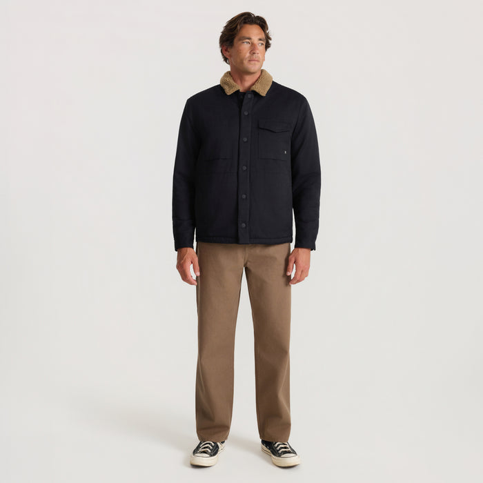 Man wearing black Hebrides 2.0 Sherpa Jacket with tan sherpa collar and chest pocket, paired with khaki pants and canvas sneakers