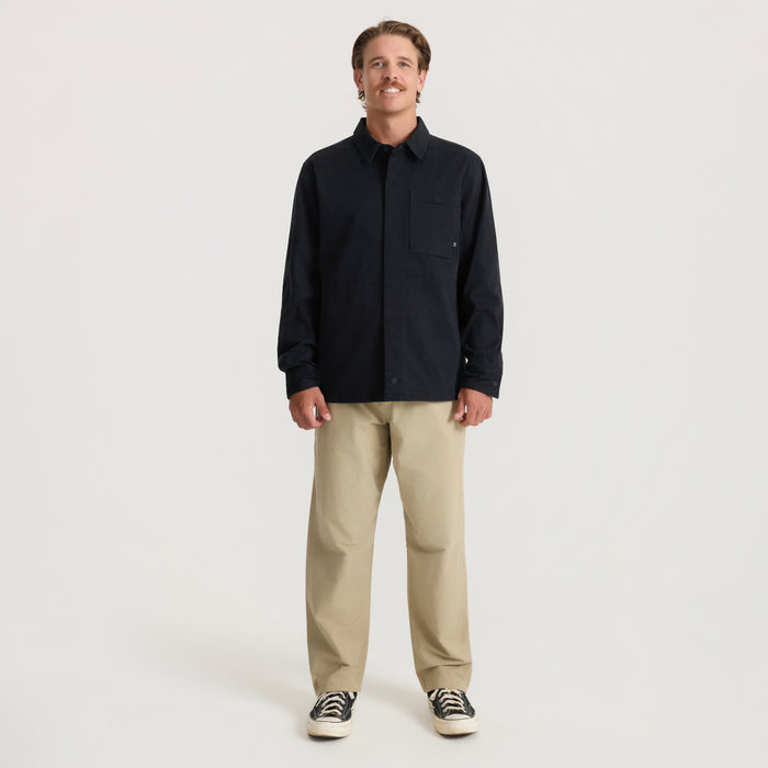 Man wearing black Hebrides 2.0 unlined jacket with khaki pants and black canvas sneakers, standing against neutral background