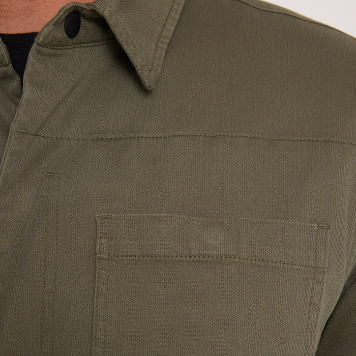 Hebrides 2.0 unlined jacket in military green with collar and chest pockets, worn on model with layered clothing