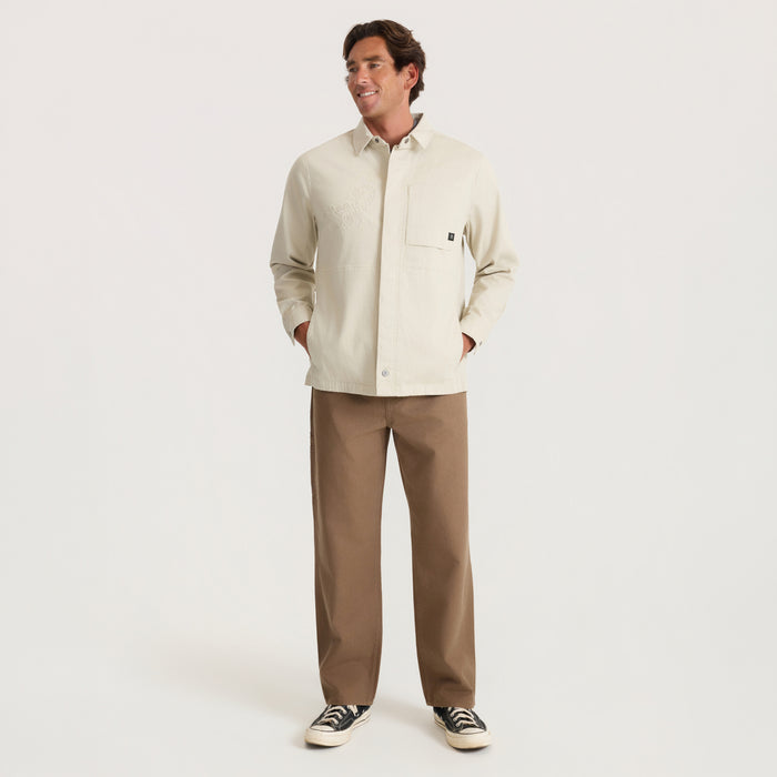 Man wearing sand-colored Hebrides 2.0 unlined jacket with chest pocket, paired with tan pants and dark sneakers
