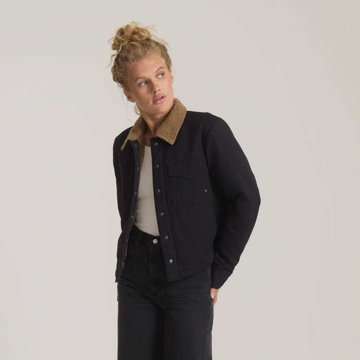 Black Hebrides Sherpa jacket with tan fleece collar worn over cream top on model paired with dark denim jeans