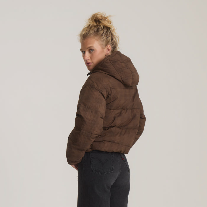 Brown quilted puffer jacket with hood on model wearing dark jeans, shown from side angle