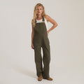 Olive green cotton overall jumpsuit with adjustable shoulder straps and front pockets, styled with white tank top on model