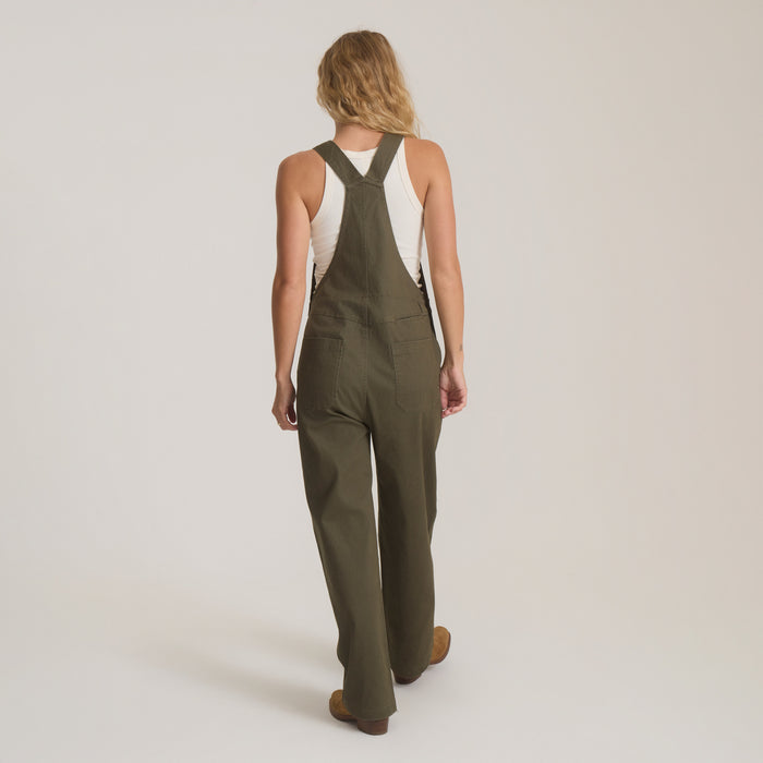 Woman wearing olive green Hwy 1 overall jumpsuit with white tank top, shown from back view with full-length silhouette
