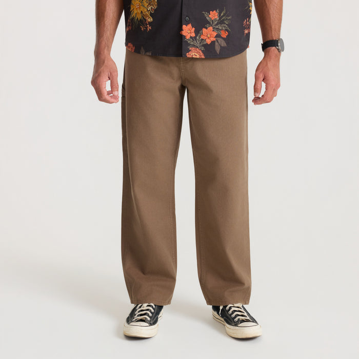 Man wearing tan HWY 1 Utility Denim jeans with black floral shirt and black canvas sneakers, shown full length from waist down