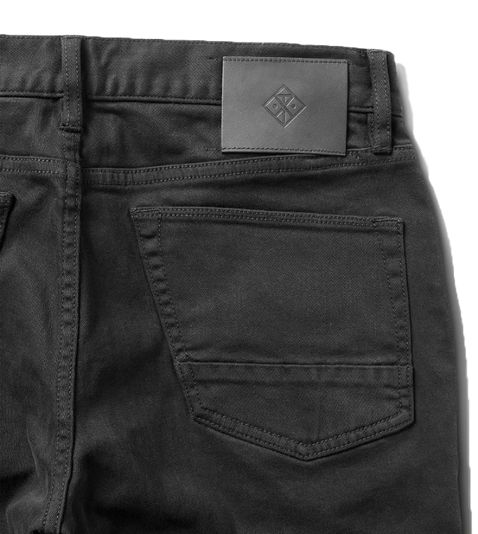 Black five-pocket denim jeans with gray leather brand label visible at waistband, detail shot showing back pocket and stitching