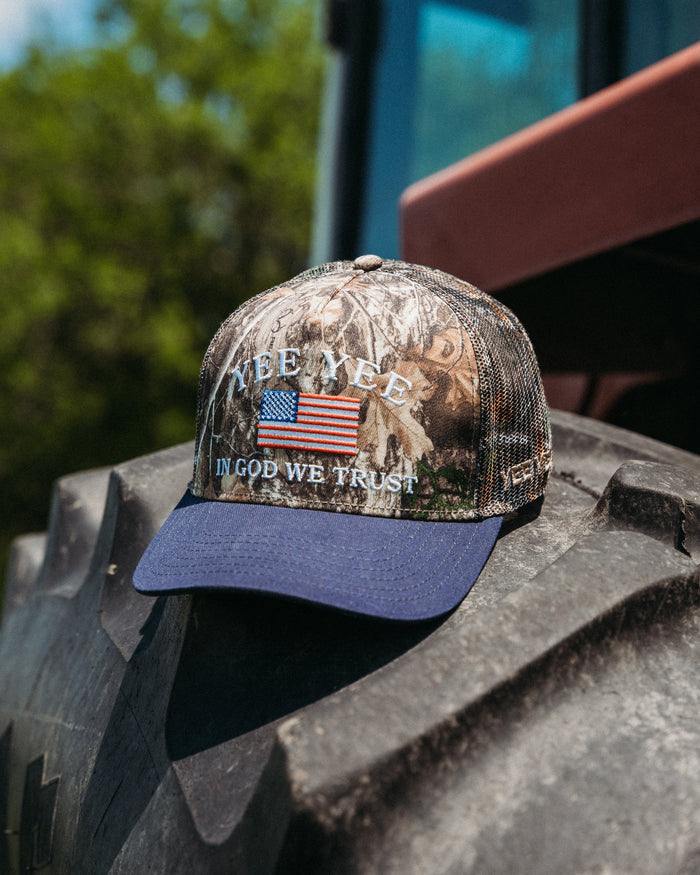 Camouflage cap with American flag and text on a tractor tire