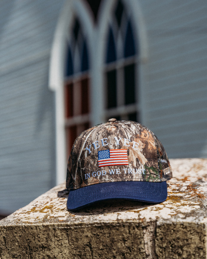 Camouflage cap with American flag and text on a wooden surface