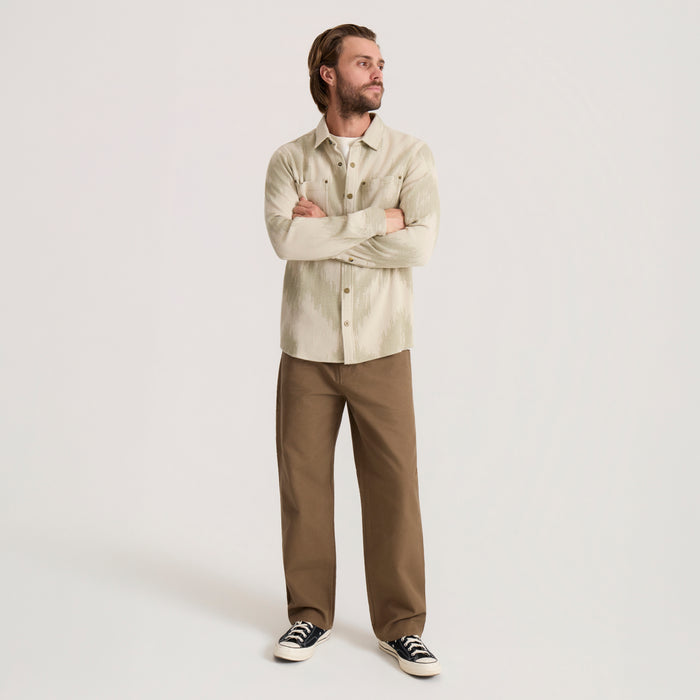 Man wearing oat-colored Journey Jacquard long sleeve flannel shirt with brown pants and black canvas sneakers, arms crossed