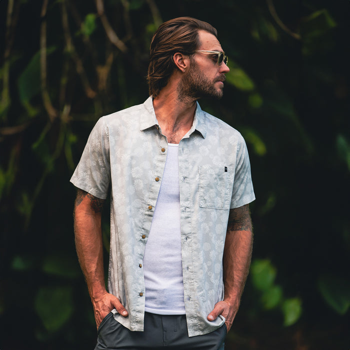 Light grey patterned short sleeve button up shirt worn by man over white undershirt in outdoor garden setting