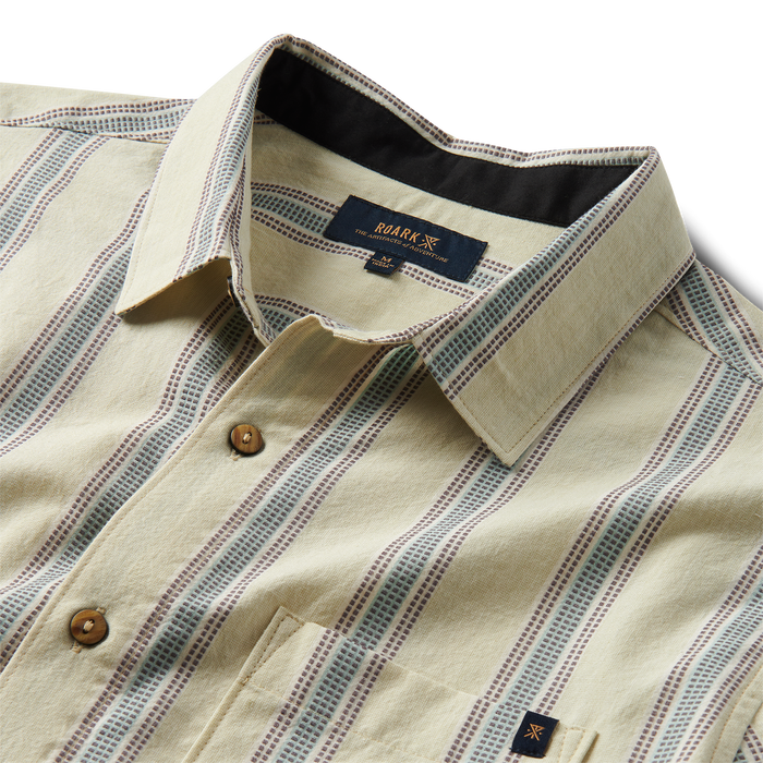 Close-up detail of a Roark dress shirt featuring distinctive buttons, sharp collar, unique design, and branded label, perfect for both adventure and travel.