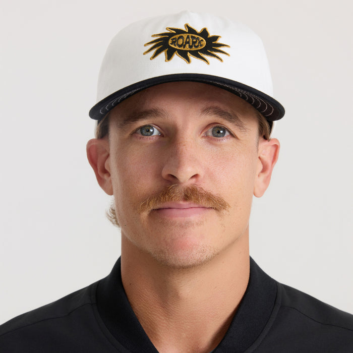 White and black snapback hat with gold embroidered Roark sun logo, worn by model against neutral background