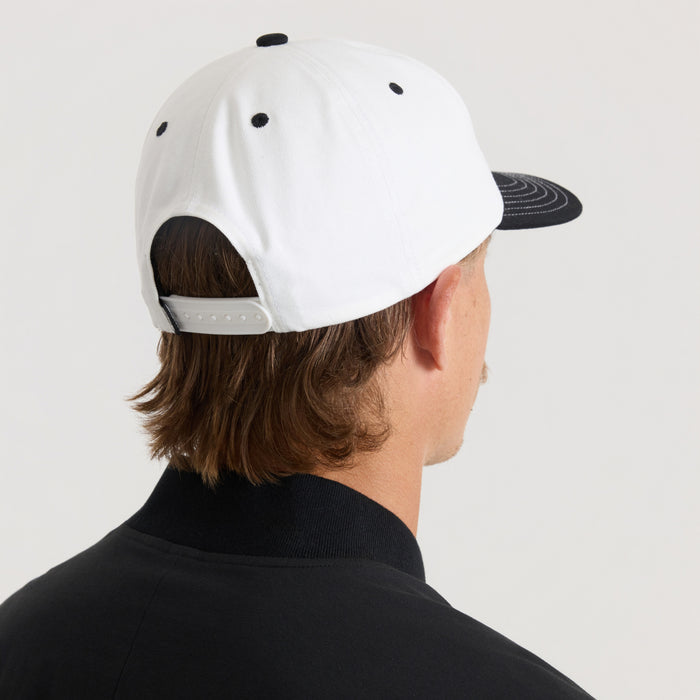 White and black Journey snapback hat worn by model shown from back angle, displaying white crown with black eyelets and black curved visor