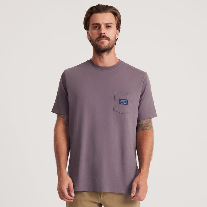 Roark presents a relaxed fit short-sleeve t-shirt in a muted purple hue, featuring a chest pocket adorned with a stylish Roark label, ideal for casual adventures.