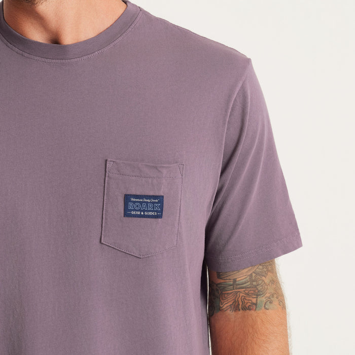 A close-up of the chest pocket on Roark’s t-shirt highlights the detailed label, blending functionality with a touch of rugged charm.