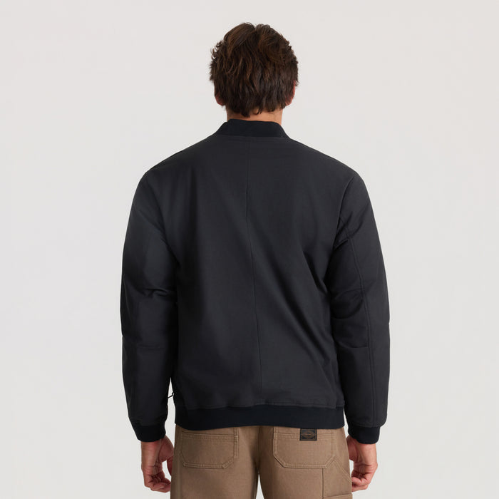 Man wearing black Layover Bomber Jacket shown from behind, paired with tan cargo pants against neutral background