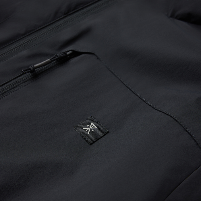 Black Layover Jacket with full-length zipper and woven brand logo patch detail, flat lay close-up view