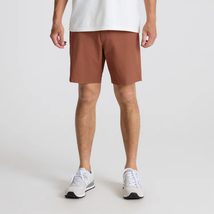 Man wearing rust-brown Layover Pro Traveler Shorts paired with white sneakers in full-body lifestyle shot