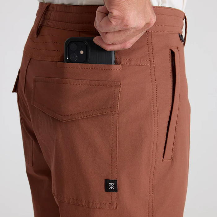 Rust-brown Layover Pro Traveler Shorts worn by model, showing back pocket with phone and cargo design detail