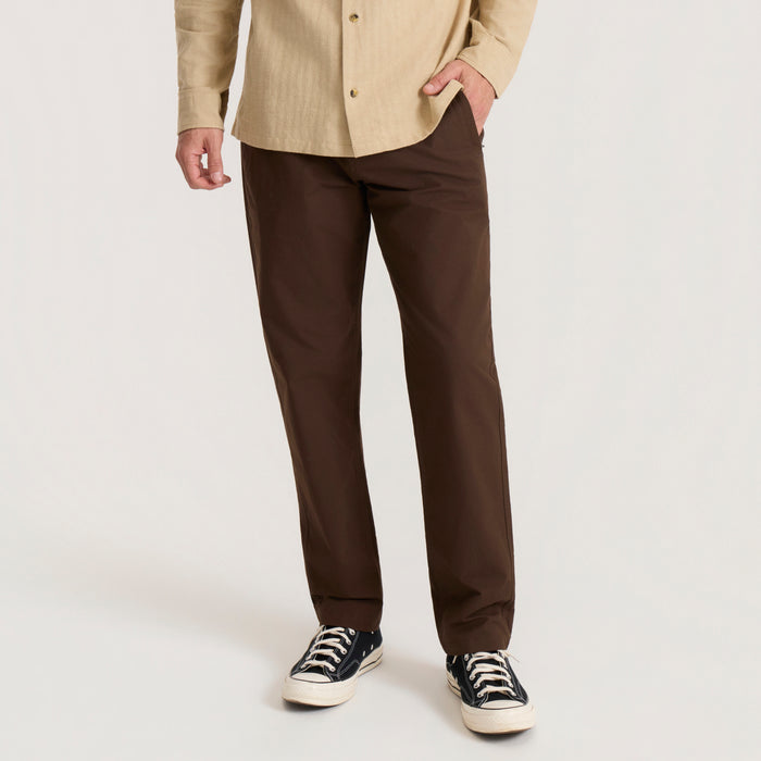 Layover Pro Traveler Pants in tobacco brown worn by model with beige shirt and navy canvas sneakers