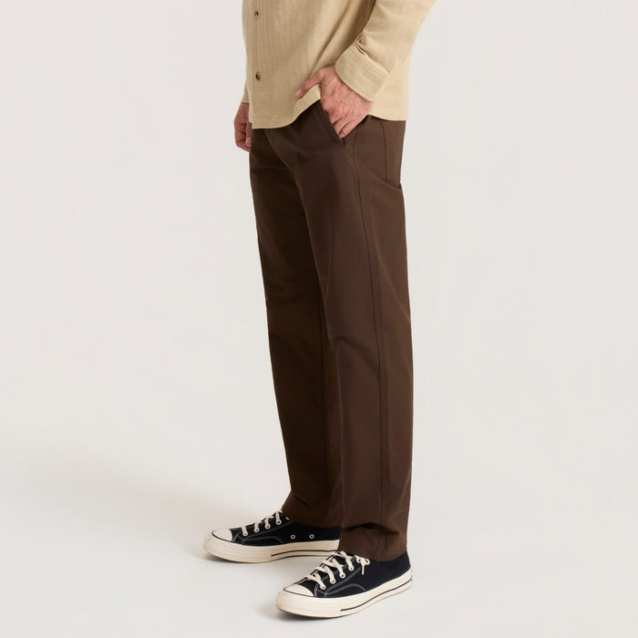 Layover Pro Traveler Pants in tobacco brown worn on model with cream button-up shirt and black canvas sneakers, side view