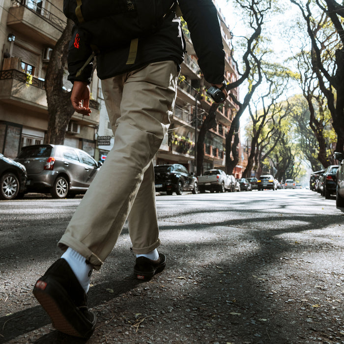 Beige Layover Trail Pants worn on model walking down urban street lined with trees and parked cars
