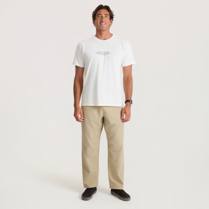 Man wearing white short-sleeve t-shirt and beige Layover Trail Pants, standing against neutral background