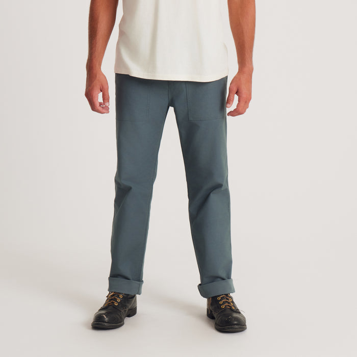 A man stands confidently in Roark's utility pants, showcasing a relaxed fit and modern design, paired with a classic white t-shirt and stylish boots.