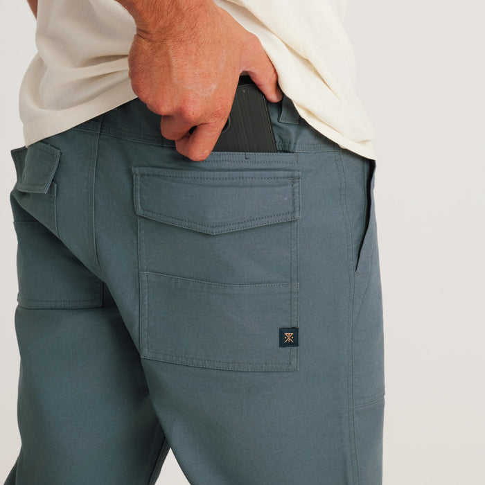 Close-up of the man's hand reaching into the pocket of his Roark utility pants, showcasing the pants' practical features for everyday use.