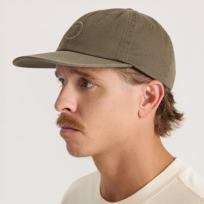 Washed military green six-panel strapback hat worn by man in side profile view, showing curved brim and embroidered logo detail