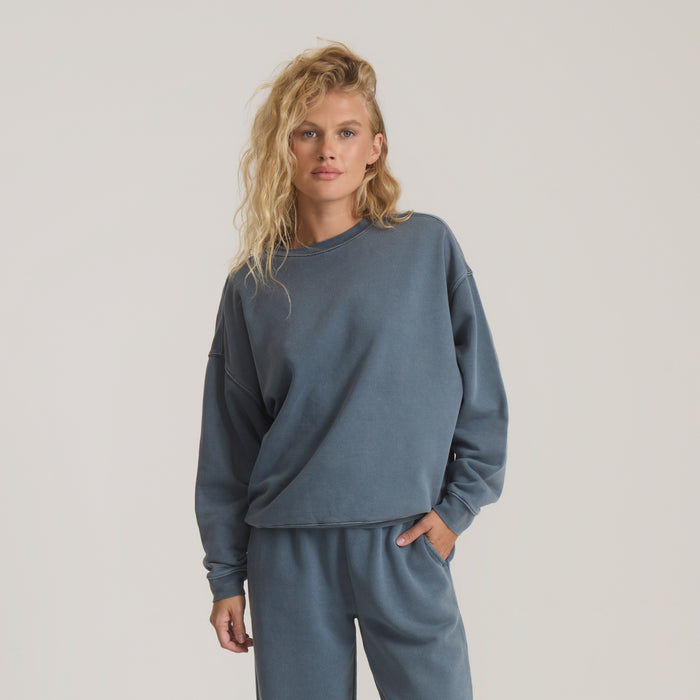 Slate blue fleece sweatshirt on model with blonde wavy hair, paired with matching joggers, full body front view